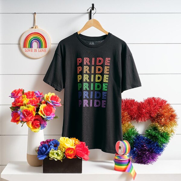 black pride t-shirt on hanger with rainbow decor on white table